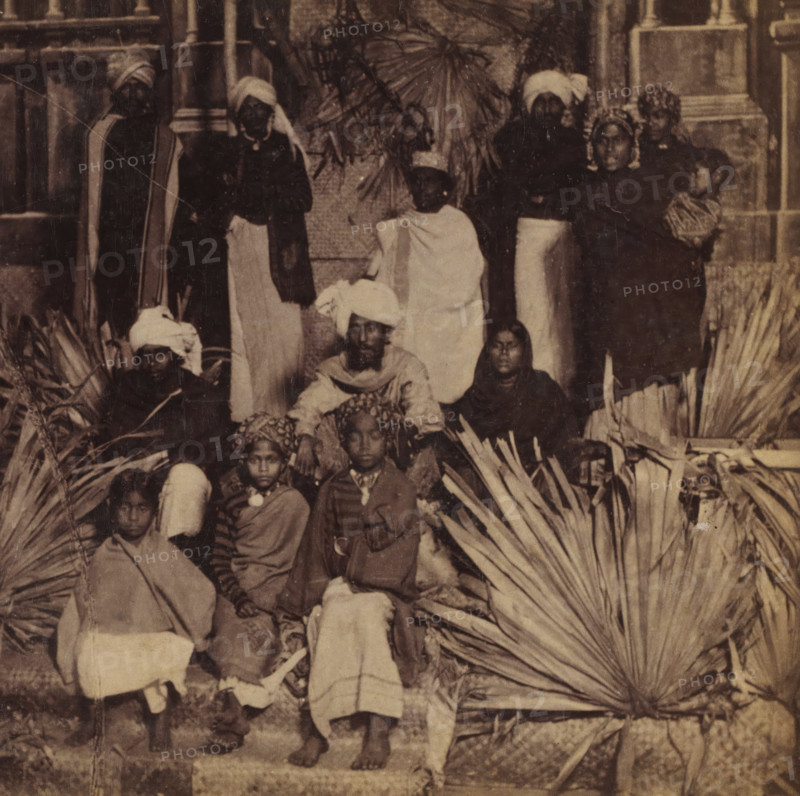 Group portrait with persons in India, Hindus, Faces and landscapes in Europe, Africa and Asia, Geographical Sculpture Gallery, collected by MJ Broekhuijsen, Head of a school in Amsterdam, stereograph, Numbered C9. bottom left of photo, annotation: 'Together with the Dravida tribes (see pl. 10), they form the principal component of the population of India. Both the Hindus and by far the majority of the Dravidas are gentle, patient, submissive people. Many distinguish themselves by an admirably beautiful physique, appearing just as beautifully in their distinctive attire as the fineness and regularity of their facial features beneath the richly pleated turban. Agriculture provides them with food (not in abundance), and the Hindu needs not much more than that. Among the Dravidas the desire for ostentation still prevails, and many a Tamil girl carries a fortune on her head, arms, and legs, carrying gold and silver with her.', annotation: 'Voor-Indië', India, publisher: Merkelbach & Co., Am...