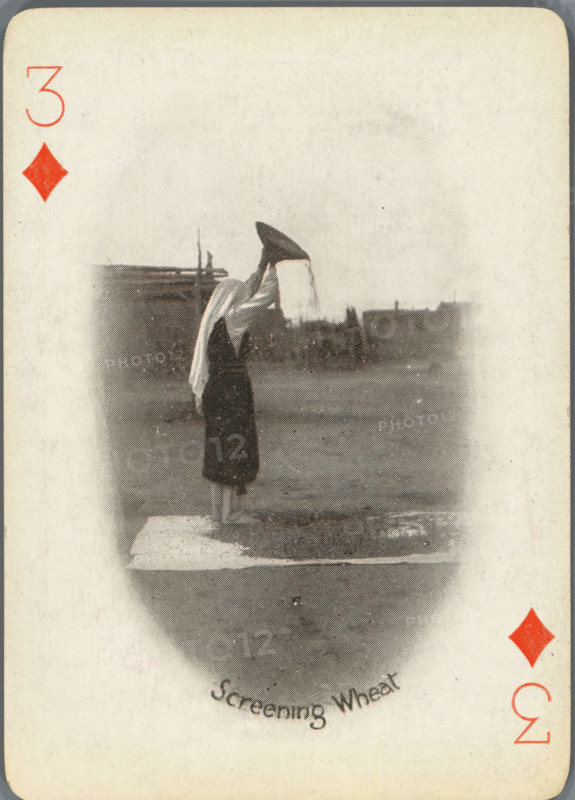 Screening Wheat, Three of Diamonds with woman separating wheat from chaff, photograph, playing card, Playing card from a box of 53 playing cards with autotype images of Native Americans. The contents include a complete set of playing cards including a joker., photographer: Adam Clark Vroman, United States of America, publisher: Lazarus & Melzer, Los Angeles (city), c. 1900, North America, paper, autotype, height 88 mm x width 63 mm, A vertically oriented playing card with rounded corners and a worn off-white background, featuring a faded oval vignette in the center that shows a person standing on a platform near water, wearing a dark skirt and a light shawl draped over the head and shoulders, holding a large conical object above their head with material falling from it; distant low buildings and a flat waterfront appear on the horizon within the vignette, and red diamond suit symbols and numerals appear near the corners of the card.