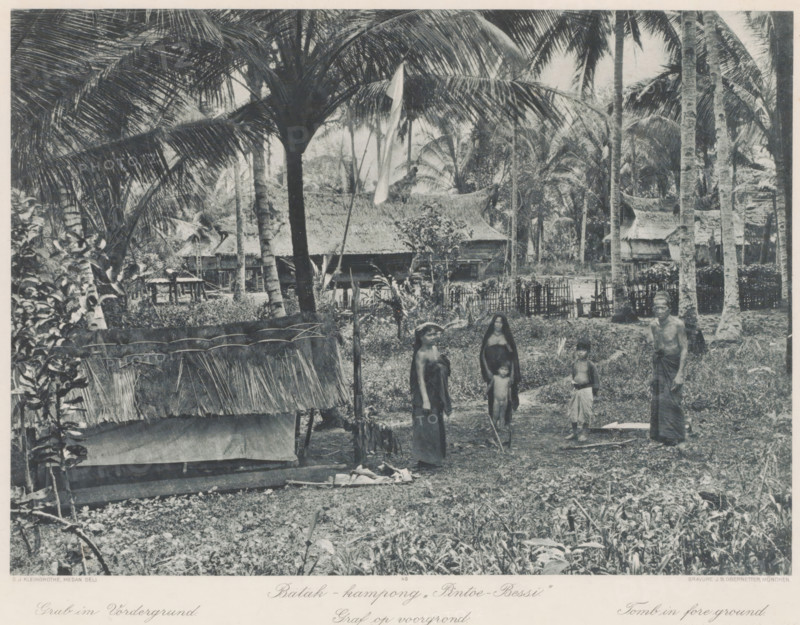 Inhabitants of Batak village 'Pintoe-Bessi' on Sumatra, with a grave in the foreground, Batak - kampong „Pintoe - Bessi' Grave in foreground, photomechanical print, Part of Album with heliogravures of Sumatra's east coast., number: '49', photographer: Carl J. Kleingrothe, Sumatra, clichémaker: Johann Baptist Obernetter, Munich, in or before 1898, Bavaria, paper, photoaquatint, heliogravure, height 207 mm x width 287 mm, grave, tomb, village, A monochrome scene shows tall palm trees with large fronds towering over a village clearing containing thatched huts and woven fences; in the foreground there is a low structure with a frayed thatch roof and scattered vegetation, and a group of people standing on the bare ground including women and children wearing simple cloth garments and a man wrapped in a cloth, all surrounded by dense tropical foliage and more traditional houses in the background.