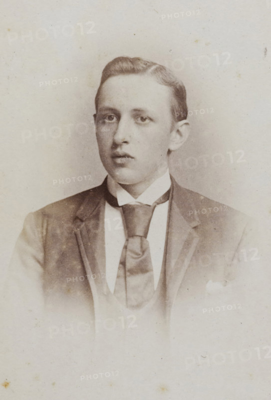 Portrait of a young man, album page, photograph, carte-de-visite, This photo is part of an album., photographer: Jan Goedeljee, Leiden, 1860 - 1905, paper, pasteboard, albumen print, albumendruk, height 83 mm x width 52 mm, historical persons, A faded sepia portrait of a young man from the chest up wearing a dark jacket over a light waistcoat and a wide cravat tied under a high white collar; his hair is neatly combed and he gazes slightly off center with a neutral expression, and the background is plain and lightly mottled.