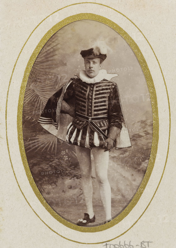 Portrait of Johannes Pieter Stephan Gualthérie van Weezel in costume, album page, photograph, carte-de-visite, This photo is part of an album., inscription: 'Ant. J. van der Stok, Leiden Rapenburg 13.', name: 'JPS Gualtherie v. Weezel., 106.', photographer: Antonius Joannes van der Stok, Leiden, 1887-01-01 - 1899-12-03, paper, pasteboard, albumen print, albumendruk, height 83 mm x width 52 mm, Person, Johannes Pieter Stephan Gualthérie van Weezel, historical persons, historical costume, An oval vintage photograph shows a person standing in theatrical attire framed by a textured mat with concentric gold rings; the person wears a dark hat with a white plume, a high ruffled collar, a patterned jacket with horizontal decorative bands and buttons, a cape draped over one shoulder with striped trim, a short skirt-like garment with alternating light and dark vertical panels, light-colored tights, and dark shoes with decorative elements; one hand rests on the hip while the other holds a small p...