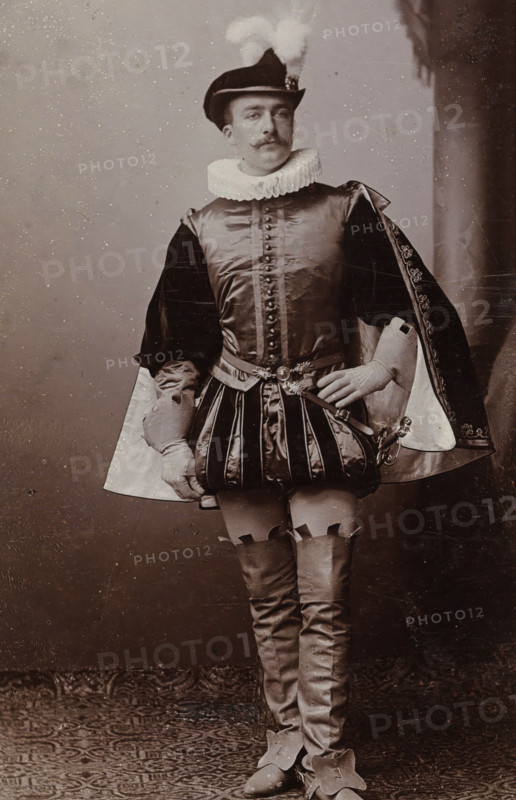 Portrait of Cornelis Hoogendijk in costume, album page, photograph, carte-de-visite, This photo is part of an album., inscription: 'J. Goedeljee, Photographer, HRH PRINCE ALEXANDER of the Netherlands, PRINCE of ORANGE, and HRH PRINCESS HENDRIK of the Netherlands, Hoogewoerd 160, near the Plantage.', name: 'C. Hoogendijk. 252.', photographer: Jan Goedeljee, Leiden, 1884 - 1894, paper, pasteboard, daylight collodion silver print, height 83 mm x width 52 mm, Person, Cornelis Hoogendijk, historical persons, historical costume, A man stands facing forward wearing a historical costume with a ruffled collar and a feathered hat, a fitted doublet with decorative buttons and a belted waist, padded trunk hose with vertical stripes, a short ornate cloak draped over one shoulder showing a patterned lining, long fitted hose with garter-like detailing at the thigh, pointed shoes with large decorative flaps, gloves on both hands, and a small sword at his side; the backdrop is plain with a textured flo...