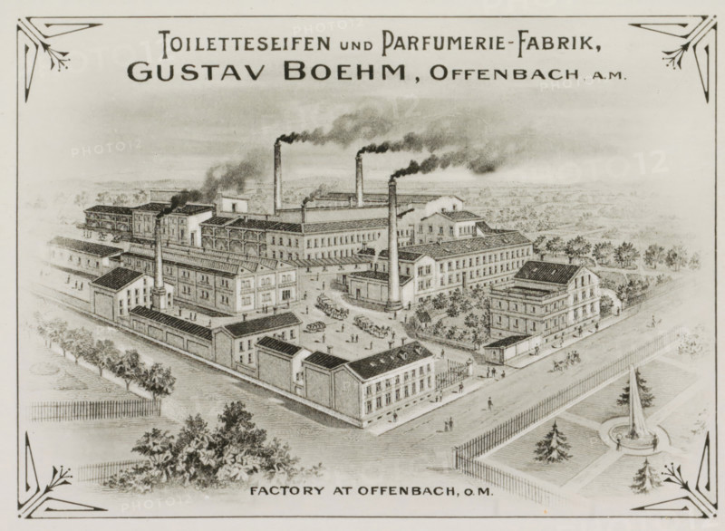 Photo reproduction of (presumably) a print of Gustav Boehm's soap and perfume factory in Offenbach am Main, photograph, reproduction, Part of Photographs of Gustav Boehm's world tour 1899-1901, series 1., after print by anonymous, 1899 - 1901, photographer, after print by, paper, gelatin silver print, developed gelatin silver print, height 82 mm x width 60 mm, factory-building, Hessen, Offenbach am Main, A detailed sepia-toned drawing of an industrial complex with multiple rectangular factory buildings arranged around courtyards, tall chimneys emitting dark smoke, small groups of people and horse-drawn carts in the open areas, rows of trees and fenced pathways surrounding the site, a street with pedestrians and a gated entrance, and decorative corner motifs framing the scene.
