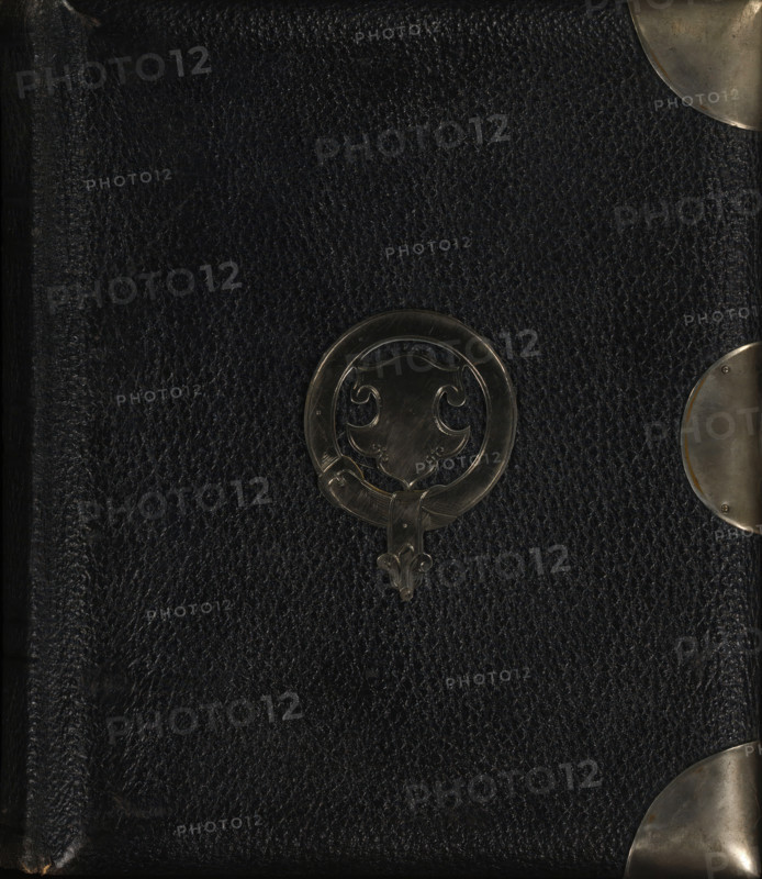 Photo album (empty), photograph album, slip-in album, Photo album with forty pages, each with a passe-partout framed with gold lines for a cabinet photo., collector's mark: 'DIENST, VERSPREIDE, RIJKSKOLLEKTIES, A 837', 1860 - 1900, pasteboard, biological material, inorganic material, paper, leather, metal, color on edges, cardboard slip-in album, covered with black leather with a metal ornament of a coat of arms in a circle on the front cover, four metal corners, metal clasp and clasp holder, decorative border printed in gold along the inside of the boards, endpapers of iridescent paper, cardboard sheets with gold edges, height 234 mm x width 205 mm x thickness 55 mm x width 399 mm, A close view of a dark textured surface with a pebbled leather appearance, featuring a circular metal ornament with an ornate shield-like design near the center and curved metallic corner protectors visible along the right edge and top right corner, the metal pieces showing a slightly worn and brushed finis...