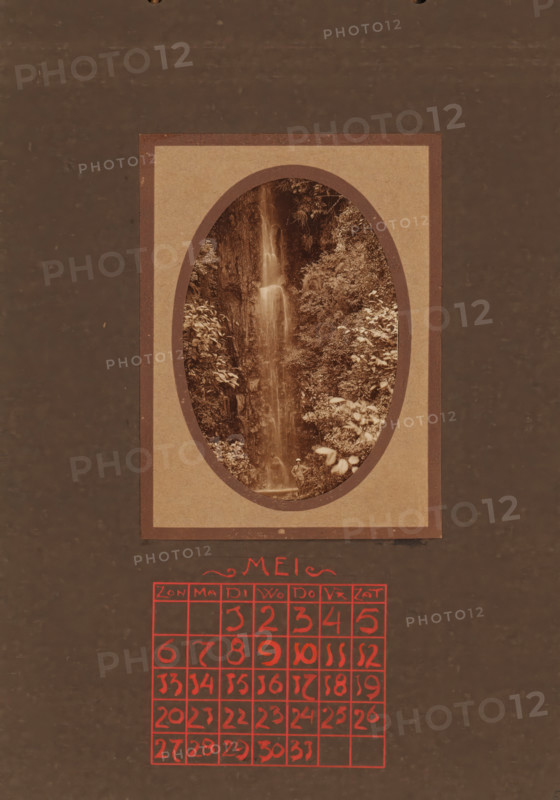 Traveler at a waterfall, album page, photograph, This photo is part of an album., annotation: 'MEI, ', Indonesia, 1880 - in or before 1923, photographer, pasteboard, paper, daylight collodion silver print, height 98 mm x width 65 mm, travelling, tourism, waterfall (landscape with figures, staffage), A vertical image with a central rectangular frame containing an oval photograph of a narrow waterfall cascading down a rocky, vegetated cliff, surrounded by dense foliage and leafy plants, and a small figure standing near the base of the waterfall; the frame is set against a dark, textured background and below the framed photograph there is a grid of hand-drawn squares filled with hand-drawn marks in a vivid color.
