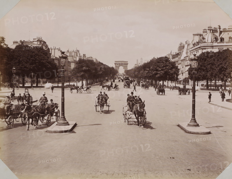 View of the Champs-Élysées with the Arc de Triomphe, album page, photograph, This photo is part of an album., retailer's mark: 'E. Hautecoeur, Estampes Photographies, 35 Avenue de l'Opéra, 35, Paris', inscription: '672 Paris - Perspective de l'Avenue des Champs-Elysées. Ed. H. Phot.', photographer: Edouard Hautecoer, Paris, publisher: Edouard Hautecoer (possibly), 1890 - 1898, Edouard Hautecoer, photographer, publisher, paper, albumen print, height 258 mm x width 355 mm, avenue, boulevard, promenade, esplanade (city(-scape) with figures, staffage), Champs-Elysées, A wide tree-lined avenue stretches toward a large stone triumphal arch at the far end, flanked by multi-story buildings with ornate roofs and chimneys. The foreground shows a broad paved roadway with horse-drawn carriages and riders moving toward and away from the viewer, and decorative lamp posts mounted on pedestals near the center. People in period clothing walk along the sidewalks and stand near the trees and carriageways...