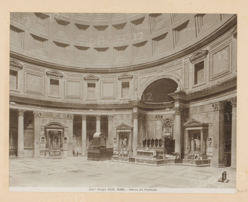 Roma - Interno del Pantheon, Interior of the Pantheon in Rome, photograph, Part of Photo album with photographs of sights and works of art in Italy., number: '4228', photographer: Edizioni Brogi, Pantheon, c. 1875 - in or before 1907, Rome, paper, gelatin silver print, height 200 mm x width 250 mm, interior of church, mausoleum, A large circular interior space with a coffered dome above and a continuous ring of rectangular recessed panels below; tall fluted columns with ornate capitals support an entablature with decorative friezes and triangular pediments above several niches; sculptural reliefs, statues in alcoves, and carved architectural details line the curved wall; an elevated altar area with balustrades and decorative furnishings sits near a semicircular arch; a freestanding structure with a curved top and a raised platform occupies the central floor area; the patterned floor shows geometric designs and the overall scene is rendered in a monochrome photographic tone.