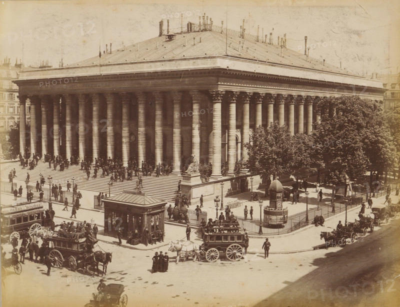 Horse-drawn trams in front of Palais Brongniart, album page, photograph, This photo is part of an album., inscription: '115 Paris_ La Bourse', photographer: X phot., 1887 - 1910, paper, albumen print, height 209 mm x width 274 mm, diligence, omnibus, horse-tram, column, pillar, architecture, façade (of house or building), Paris, Palais Brongniart, A large neoclassical stone building with a wide flight of steps leading up to a portico of tall fluted columns capped by ornate capitals fills most of the scene, a seated stone sculpture on a raised pedestal positioned at the corner of the steps, a tall low roof with many small vertical pipes and vents rising above the entablature, and rows of windows and architectural details visible along the sides. Numerous people are on the steps and around the building, some standing in groups and others walking, while horse-drawn carriages and a large enclosed omnibus occupy the street in front. A fenced plaza with trees and lamp posts sits adjacent to ...
