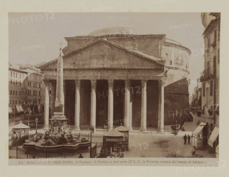View of the Pantheon and the Macuteo obelisk in Rome, Italy, Il Pantheon. Il Portico e dell' anno 27 AC, la Rotonda credesi del tempo di Adriano, Roma, photograph, number: 'Pe. Ia. No. 6688.', photographer: Fratelli Alinari, Rome, after sculpture by anonymous, 1852 - 1900, Fratelli Alinari, photographer, after sculpture by, pasteboard, paper, albumen print, height 101 mm x width 141 mm, height 167 mm x width 223 mm, church (exterior), obelisk, needle, Pantheon, A sepia-toned photograph of a classical temple façade with a triangular pediment and a row of tall fluted columns supporting an entablature, flanked by a curved rotunda wall on the right and adjacent buildings on the left, with an obelisk standing in front of the temple and a sculpted fountain basin with ornate figures at its base, street lamps and a fenced area around the fountain, awnings and shopfronts along the surrounding streets, and two figures standing on the paved street near the lower right corner.