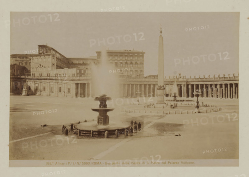 Una parta della Piazza di S. Pietro col Palazzo Vaticano, View of St. Peter's Square with the obelisk in Vatican City, Italy, Roma, photograph, In the background are the colonnades of Giovanni Lorenzo Bernini., number: 'Po. Io. No. 5903.', photographer: Fratelli Alinari, Vatican City, after sculpture by anonymous, 1852 - 1900, Fratelli Alinari, photographer, after sculpture by, pasteboard, paper, albumen print, height 97 mm x width 143 mm, height 0 mm x width 0 mm, square, circus, ornamental fountain, obelisk, needle, St. Peter's Square, A wide open paved square with a large central fountain in the foreground spraying water upward, a multi-tiered stone basin surrounded by short posts and chains, and a tall obelisk rising toward the sky further back; a curved colonnade of columns extends across the middle ground with statues lined along its top, and large stone buildings with rows of windows form the background; scattered lampposts and another smaller fountain appear near the obelisk, a...