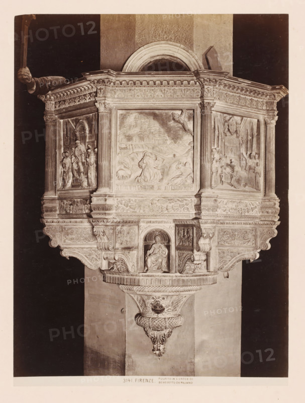 Pulpit after Benedetto da Maiano in the Santa Croce in Florence, Italy, Pulpito in S. Groce di Benedetto da Majano, Firenze, photograph, number: '3141.', address: 'GIACOMO BROGI, FOTOGRAFO-EDITORE, FIRENZE, LUNG ARNO DELLE GRAZIE 15', photographer: Giacomo Brogi, Florence, publisher: Edizioni Brogi, after sculpture by Benedetto da Maiano, 1864 - 1881, Benedetto da Maiano, after sculpture by, Tuscany, pasteboard, paper, albumen print, albumendruk, height 470 mm x width 350 mm, pulpit, ambo, chancel, Santa Croce, An ornate stone pulpit with carved panels and columns sits against a wall, featuring a central rectangular relief depicting figures and a landscape above a seated sculpted figure in a niche, flanked by two side reliefs showing groups of standing and seated figures within architectural settings, all topped by an elaborately decorated cornice with floral and geometric motifs and supported by a carved bracket with scrollwork and a textured pendant.