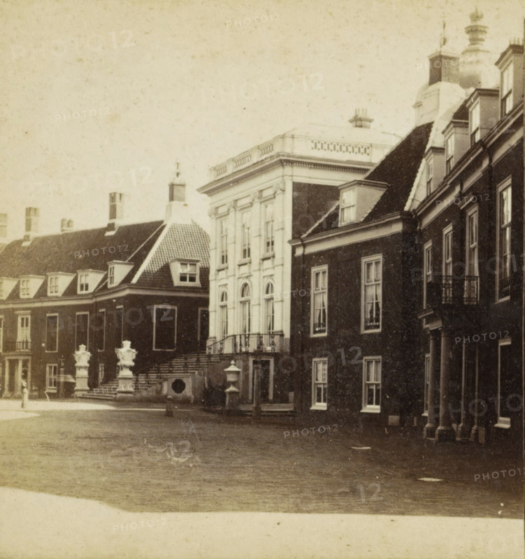 The Hague, Huis ten Bosch, View of Huis ten Bosch Palace in The Hague, stereograph, 1868 - 1890, photographer, pasteboard, paper, albumen print, albumendruk, height 85 mm x width 169 mm, palace, Paleis Huis ten Bosch, A sepia-toned street scene showing the facades of several connected buildings with tall windows and varied rooflines, including pitched and flat roofs with dormer windows and chimneys, a central lighter-colored building with ornate window frames and a balustraded roofline, stone steps leading up to an entrance flanked by decorative stone urns, iron railings along balconies and stairways, a paved open area in the foreground, and architectural details such as columns, cornices, and window sills visible across the structures.