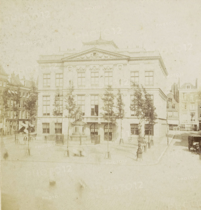The Boymans Museum., Le Musée Boymans., Das Museum Boymans., Boyman's Museum, View of the Schielandshuis in Rotterdam, Rotterdam, stereograph, 1867 - 1870, photographer, pasteboard, paper, albumen print, albumendruk, height 88 mm x width 175 mm, Person, villa, Schielandshuis, A faded photograph of a large classical building with a triangular pediment and decorative facade, tall rectangular windows arranged across multiple stories, and a central entrance with arched doorways; trees stand in front of the building partially obscuring the lower windows, flanking a statue on a pedestal near the entrance; surrounding the main structure are adjacent narrower buildings with multiple windows and varied rooflines; in the foreground a paved open area shows lamp posts and low bollards, and a horse-drawn carriage is visible to one side, with faint figures and street details scattered across the scene.