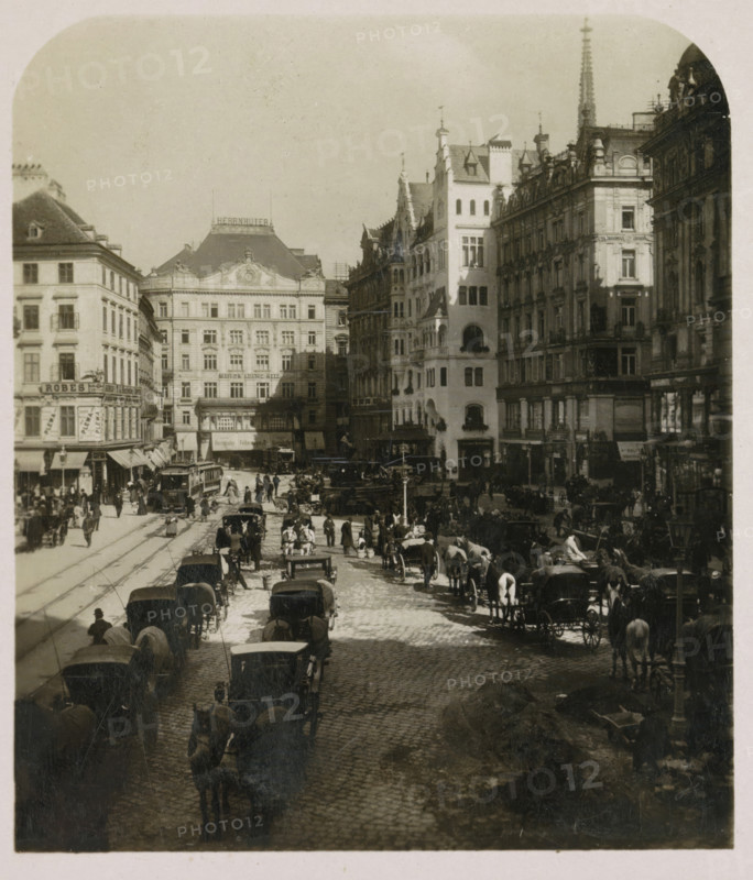 Neuer Markt in Vienna, seen towards the north, Neuer Markt, Wien, stereograph, number: '4549', number: 'No. 4549', Vienna, publisher: Würthle & Sohn, Salzburg (city) (possibly), 1908 - 1909, photographer, Lower Austria, paper, baryta paper, gelatin silver print, developing gelatin silver print, height 90 mm x width 177 mm, square, circus, Hoher Markt, A wide street scene filled with horse-drawn carriages and pedestrians between tall ornate buildings, cobblestone pavement visible under the vehicles, a tram with tracks and people waiting, multi-story facades with decorative architectural details and windows, a taller lighter-colored corner building with arched openings, crowds of people clustered along sidewalks and crossing the street, numerous horses hitched to carriages lining both sides of the road, lampposts and street furniture, and a distant building with a pitched roof and ornamental rooftop features.