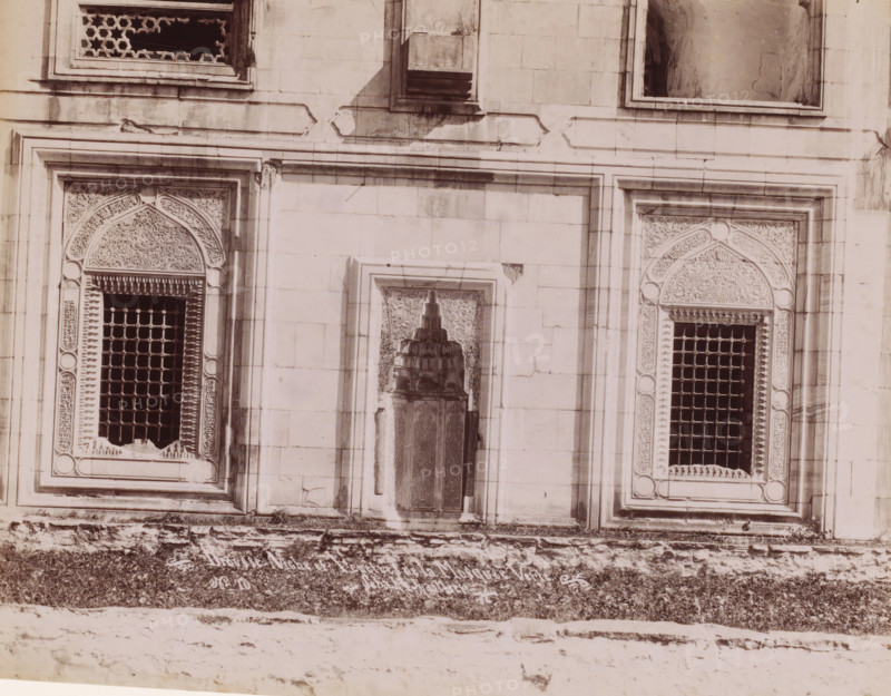 Brousse, niche et fenêtre de la Mosquée Verte, Façade of the Green Mosque in Bursa, photograph, number: 'No 70', photographer: Sébah & Joaillier, Bursa, 1888 - 1900, paper, albumen print, height 210 mm x width 268 mm, temple, shrine, Islam, Mohammedanism, Green Mosque, A section of a stone building facade with three framed recessed panels, two of the outer panels containing arched ornamental stonework and metal grilles, and a central recessed niche with a carved decorative fountain element; the stone surface shows weathering and stains, and the rectangular framing around each panel has raised molding; the lower edge of the image shows a rough stone ledge and textured ground.
