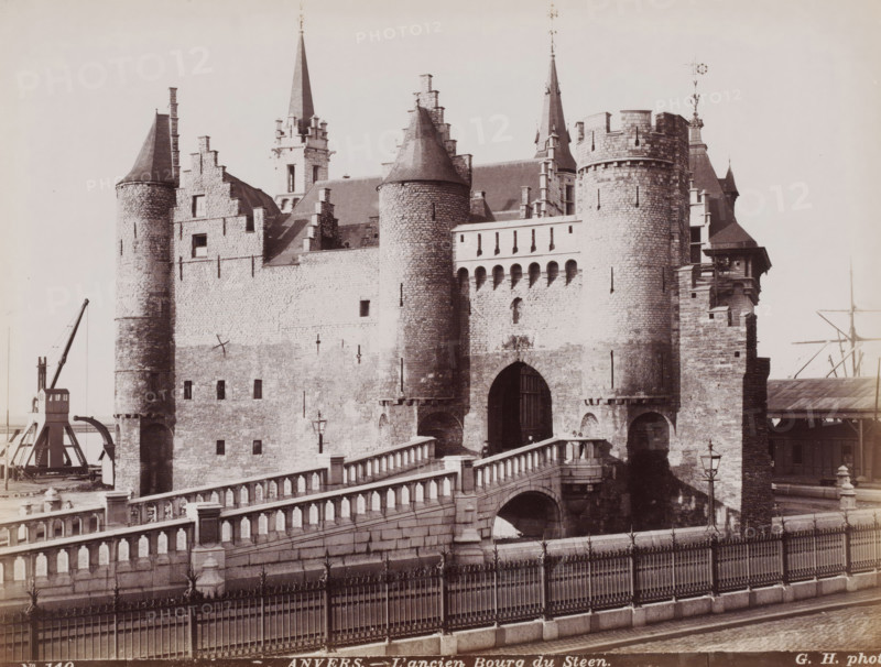 The old town of Het Steen, View of Het Steen in Antwerp, Belgium, Anvers, photograph, number: 'No 140', photographer: Gustave Hermans, Antwerp, 1884 - 1914, paper, albumen print, height 215 mm x width 281 mm, castle, Het Steen, A stone fortress with rounded towers and crenellated walls stands behind a stone balustraded bridge, showing arched gateways and narrow slit windows; steep conical roofs and tall spires rise above the masonry, and a metal fence runs along the foreground beside a cobbled street; a crane structure and parts of a dock are visible at the left and right edges.