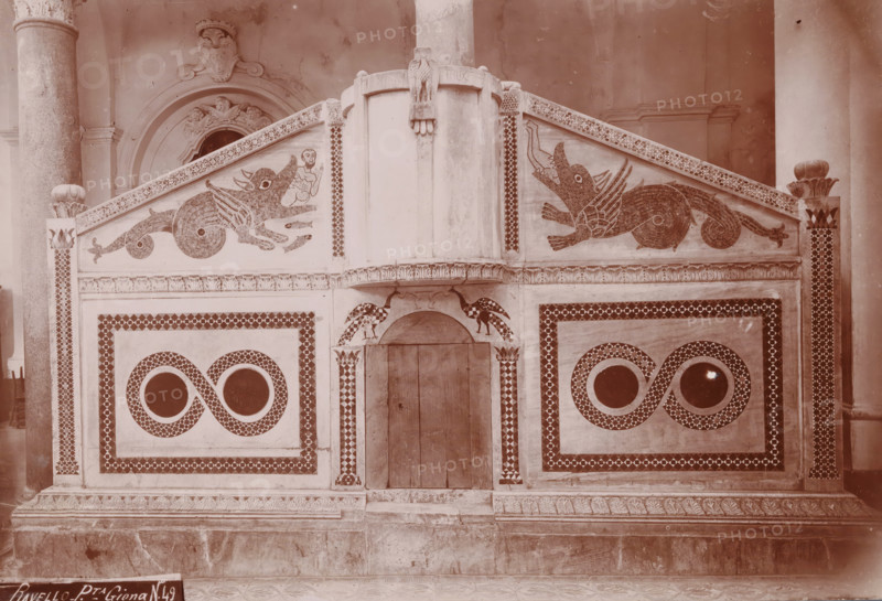 Ravello - Pta. Giona, Pulpit in the cathedral of Ravello, photograph, number: 'N. 49', Ravello, 1880 - 1920, photographer, paper, daylight gelatin silver print, height 141 mm x width 260 mm, pulpit, ambo, chancel, Dom (Ravello), A decorative stone or plaster façade with symmetrical rectangular panels and patterned borders fills the image, featuring two stylized winged creatures facing inward along the upper sloped panels and a small human-like figure near one creature, a central vertical column with a carved eagle at its top, arched recessed doorway beneath the column flanked by bird motifs, circular window-like openings set inside figure-eight patterned designs on each lower panel, fluted columns visible at the far left and right edges, and carved ornamental molding and a patterned base along the bottom.