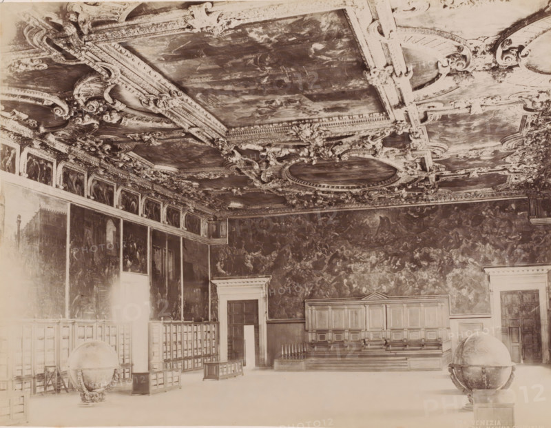 Hall of the Great Council in the Doge's Palace in Venice, Italy, Salle del maggior consiglio, Venezia, photograph, number: '154 ?', Venice, 1851 - 1900, photographer, pasteboard, paper, albumen print, albumendruk, height 323 mm x width 373 mm, globe, palace, (decorated) ceiling, Doge's Palace, A large ornate interior with a richly decorated ceiling featuring carved moldings and painted panels, walls covered with large-scale paintings, a raised wooden platform with paneled seating and a decorative railing, tall doors set into paneled wall sections, freestanding globes on carved stands placed on the floor, and rows of wooden partitions and small display cabinets along one side.