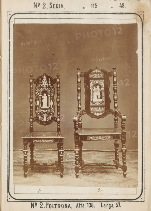 Two chairs with inlaid decorations, No 2 Sedia, Poltrona, photograph, page, inscription: '' 115 ' 48., Alta, 138. Larga, 57.', inscription: 'No. 1. Fes. 60, ' 2 ' 100', c. 1878 - c. 1885, photographer, paper, albumen print, albumendruk, height 126 mm x width 98 mm, Photo on unnumbered page., chair, Two ornate wooden chairs are shown side by side against a plain backdrop with a patterned floor beneath them. Each chair features a tall decorative back with turned vertical posts and intricate carved panels that include framed figurative images. The seats are flat with inlaid or painted decorative motifs along the front apron and the legs are turned with carved details and small embellishments. The chair on the right has armrests with carved supports extending from the seat to the arm, while the chair on the left lacks arms and has a slightly narrower back panel. A rectangular border surrounds the image and a narrow margin of aged paper with small spots is visible at the edges.