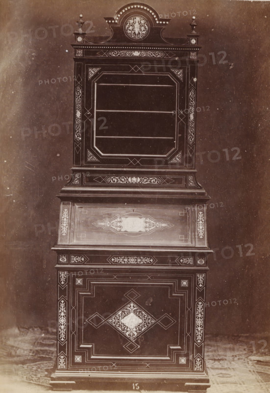 Ivory inlaid case, No 15 Mobile Avorio, photograph, page, inscription: 'Alto, 178. Largo, 79. Fondo, 55.', inscription: 'Ies. 360', c. 1878 - c. 1885, photographer, paper, albumen print, height 135 mm x width 97 mm, Photo on unnumbered page, ornamental cupboard, A tall ornate wooden cabinet photographed against a plain backdrop, showing upper and lower sections with decorative inlaid patterns and geometric borders; the top has a crowned pediment with a round medallion featuring a floral motif flanked by small urn finials, below which is a framed recessed display area with horizontal shelves and corner triangular panels filled with intricate scrollwork; a middle slanted panel displays a central ornamental cartouche surrounded by narrow borders, and the lower doors feature a large central diamond-shaped medallion with floral inlay and surrounding rectangular stepped panels; narrow vertical pilasters with repeating floral inlays run along the sides, and the cabinet rests on a short molded...