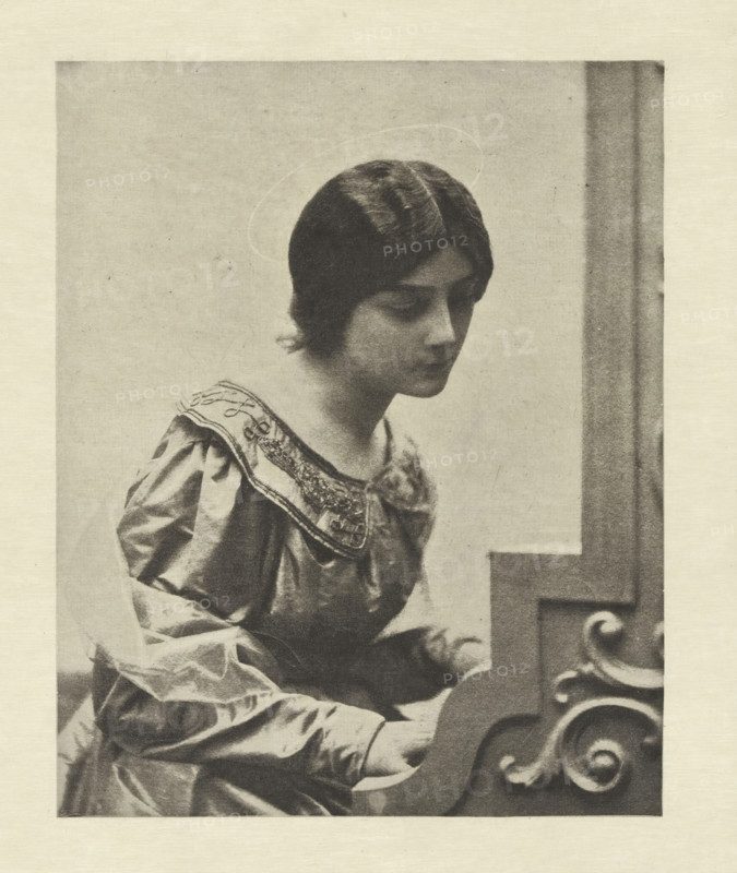 Portrait of an unknown woman as Saint Cecilia, Sainte Cécile, photomechanical print, photographer: Adolphe Gayne de Meyer, cliché maker: Fillon & Heuse, printer (person): Charles Wittmann, Paris, c. 1891 - in or before 1896, printer (person), paper, photoaquatint, height 158 mm x width 127 mm, historical persons not known by name - BB - woman, the virgin martyr Cecilia of Rome, possible attributes: falcon, musical instruments, organ, wreath of roses and lilies, A monochrome image of a young woman shown from the waist up, seated and facing slightly right with her head inclined downward, wearing a dress with a decorated collar and puffed sleeves, her hair parted in the middle and styled close to her head, a faint circular halo-like outline appears above her head, and the right side of the image shows a portion of a carved wooden structure with scrollwork near where her hands rest.