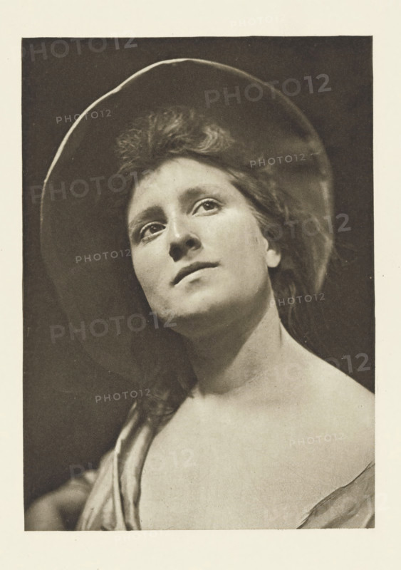 Marcelle, Portrait of an unknown young woman named Marcelle, photomechanical print, photographer: Robert Pauli, cliché maker: Fillon & Heuse, printer (person): Charles Wittmann, Paris, c. 1891 - in or before 1896, printer (person), paper, photoaquatint, height 175 mm x width 125 mm, historical persons not known by name - BB - woman, adolescent, young woman, maiden, A sepia-toned portrait of a young woman shown from the shoulders up wearing a wide-brimmed hat, her head tilted slightly upward and to the side, with loose hair framing her face and a soft, contemplative expression, visible eyes looking upward, a straight nose, closed lips, bare shoulders, and part of a draped garment over one shoulder, set against a dark background with a light border around the image.