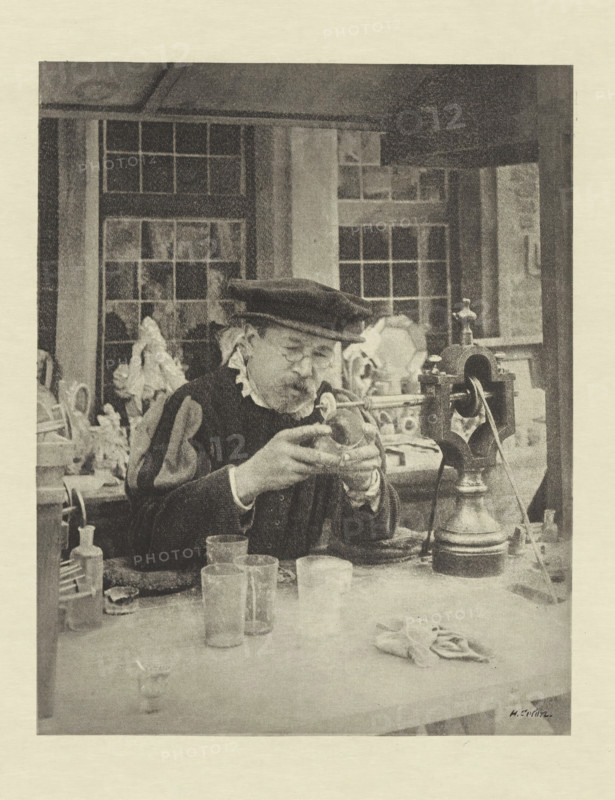 Le Graveur sur fout, Man engraves on glass, photomechanical print, photographer: Henri Colon, cliché maker: Fillon & Heuse, printer (person): Charles Wittmann, Paris, c. 1891 - in or before 1896, printer (person), paper, photoaquatint, height 179 mm x width 142 mm, handicrafts, glass, An older man wearing a dark beret and round glasses sits at a cluttered workbench, holding a small object close to his face with both hands while looking down; he wears a dark garment with a light ruffled collar and sleeves, and a patterned sleeve is visible on one arm. Around him on the bench are several glass beakers and bottles, a cloth, and various tools, and to his right is a large ornate device with a rounded base and a vertical spindle. Behind him are tall multi-paned windows and shelving with indistinct objects, and the scene is rendered in a grainy monochrome texture.
