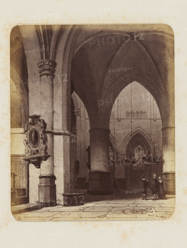 Photo reproduction of the painting 'In the Church in Haarlem' by Jan Jacob Schenkel, photograph, reproduction, page, photographer: Binger & Chits, after painting by Jan Jacob Schenkel, c. 1866 - in or before 1871, paper, albumen print, height 163 mm x width 137 mm, interior of church, Haarlem, A sepia-toned interior view of a vaulted stone building showing tall rounded columns and ribbed arches, with a decorative carved wall plaque mounted on one column, hanging chandeliers shaped like boats suspended from the ceiling, a tiled floor with visible stone seams and a circular decorative floor motif, and a small group of three people standing and conversing near one of the columns.