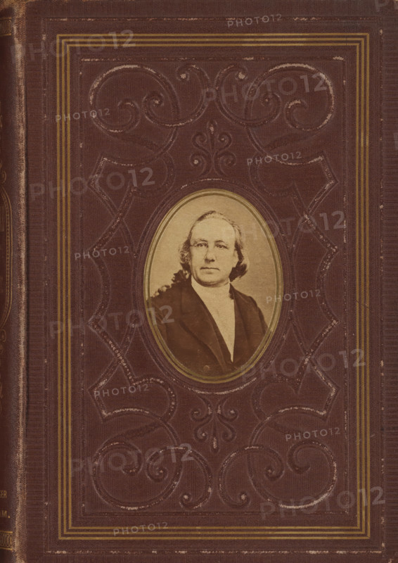 Portrait of Johannes Petrus Hasebroek, photograph, c. 1869 - in or before 1874, photographer, paper, albumen print, albumendruk, height 67 mm x width 48 mm, Photo on outside front cover., Person, Johannes Petrus Hasebroek, picture, painting, A worn brown book cover with embossed decorative scrollwork and a rectangular border of thin gold lines surrounding an oval inset photograph of a middle-aged person with light-colored hair, wearing a dark coat and a light shirt, the oval photograph framed by a thin gold rim and positioned near the center of the cover.