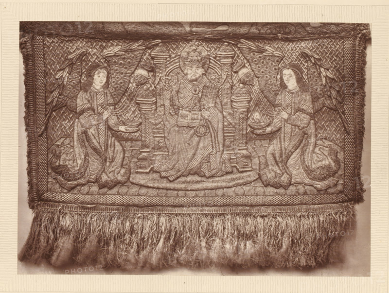 Part of an embroidered pall, A portion of a pall, page, photomechanical print, number: 'NO. 53.', inscription: 'Lent by the Fishmongers' Company', photographer: Isabel Agnes Cowper, United Kingdom, cliché maker: anonymous, after design by anonymous, c. 1869 - in or before 1874, Isabel Agnes Cowper, photographer, cliché maker, after design by, paper, Woodburytype, Woodburytypepie, height 148 mm x width 207 mm, (other forms of) needlework, eg: crocheting, knitting, embroidering, A rectangular woven textile panel with a fringed lower edge is shown; the panel features an ornate central scene with a seated figure wearing a tall rounded headdress and holding an open book, flanked by two kneeling figures in flowing robes and veiled heads, each holding shallow bowls and standing before decorative columns and patterned backgrounds; large stylized wings or feathered motifs extend behind the kneeling figures, and the panel is bordered by textured bands and tasselled edges with dense fringe hangin...