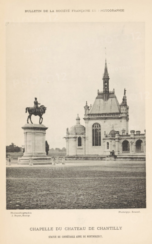 Chapelle du Chateau de Chantilly, Equestrian statue and chapel of Château de Chantilly, page, photomechanical print, inscription: 'Sstatue du connétable Anne de Montmorency', photographer: H. Rouxel, Chantilly, cliché maker: Jules Royer, after sculpture by anonymous, Nancy, c. 1886 - in or before 1891, after sculpture by, printer (person), paper, collotype, photoprint, height 158 mm x width 118 mm, Print on unnumbered page., equestrian statue, church (exterior) - QQ - small church, chapel, Château de Chantilly, A sepia-toned photograph showing a large open gravel foreground leading to a raised stone pedestal topped by an equestrian statue on the left and a gothic chapel building on the right, the statue depicting a rider seated on a horse, the chapel featuring a tall central spire, arched windows, ornate roofline details, small domed chapel sections and colonnaded facades, with low boundary posts in front of the pedestal and distant trees visible along the horizon.