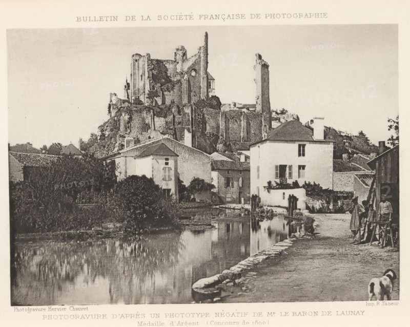 Château de Chantilly, seen from the garden side, Chateau de Chantilly (Coté des Jardins), page, photomechanical print, photographer: H. Rouxel, Chantilly, cliché maker: Jules Royer, Nancy, c. 1886 - in or before 1891, printer (person), paper, collotype, photoprint, height 120 mm x width 171 mm, Print on unnumbered page., castle, A riverside scene shows a stone embankment and a calm reflective body of water in the foreground with buildings and vegetation along the far bank, including a pale multi-story house with shuttered windows and a doorway opening onto the water. Behind these houses a large ruined stone structure with tall battered walls and towers rises on a rocky hill. Trees and shrubs grow among the buildings and ruins. On the right a narrow dirt path runs beside the water where a woman in a long dress and a man in simple clothing stand near a wooden cart, and two dogs walk along the path toward the foreground. The sky above is clear and pale.