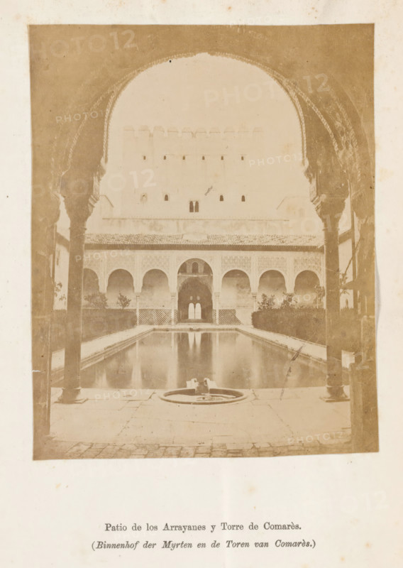 Court of the Myrtles and the Tower of Comarès in the Alhambra, Patio de los Arrayanes y Torre de Comarès, Court of the Myrtles and the Tower of Comarès, photograph, page, Granada, c. 1875 - in or before 1880, photographer, Andalusia, paper, albumen print, height 121 mm x width 96 mm, courtyard, Alhambra, A sepia-toned photograph showing a rectangular courtyard with a long reflective pool extending toward an arched colonnade, framed in the foreground by ornate archways and columns on both sides. The far wall features a row of decorative arches above a tiled lower section and a central doorway with a double-arched opening that reflects in the pool. Low hedges and small trees line the sides of the courtyard behind the pool, and a circular fountain element sits at the near edge of the water on a stone paving surface. The image has a faded, aged appearance with visible grain and uneven toning.