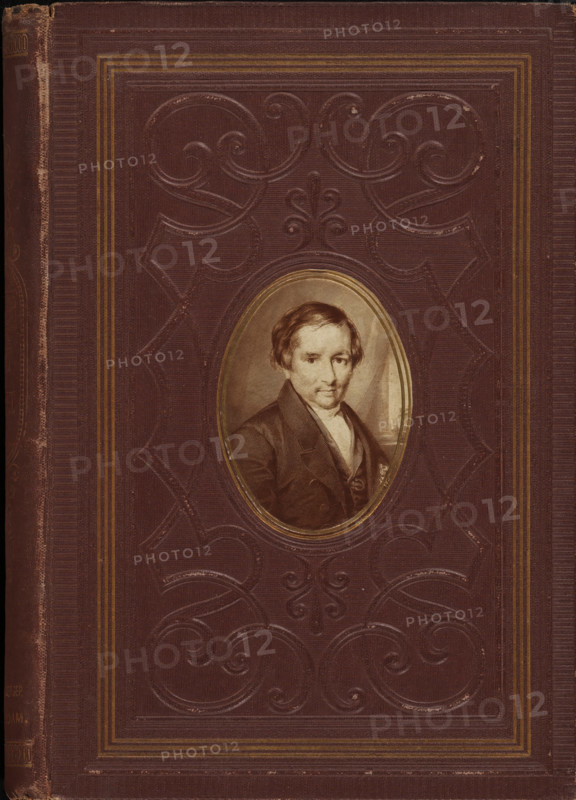 Photo reproduction of an engraving of a portrait of Johannes Petrus Hasebroek, photograph, reproduction, page, after print by anonymous, c. 1869 - in or before 1874, photographer, after print by, paper, albumen print, height 67 mm x width 49 mm, Photo on front cover., Person, Johannes Petrus Hasebroek, historical persons, A worn dark brown book cover with embossed scrolling decorative patterns and several narrow parallel border lines in a lighter brown or gold tone, featuring an oval portrait inset near the center showing a seated man with short hair wearing a dark coat and light-colored shirt, the portrait framed by a thin metallic-looking oval border.