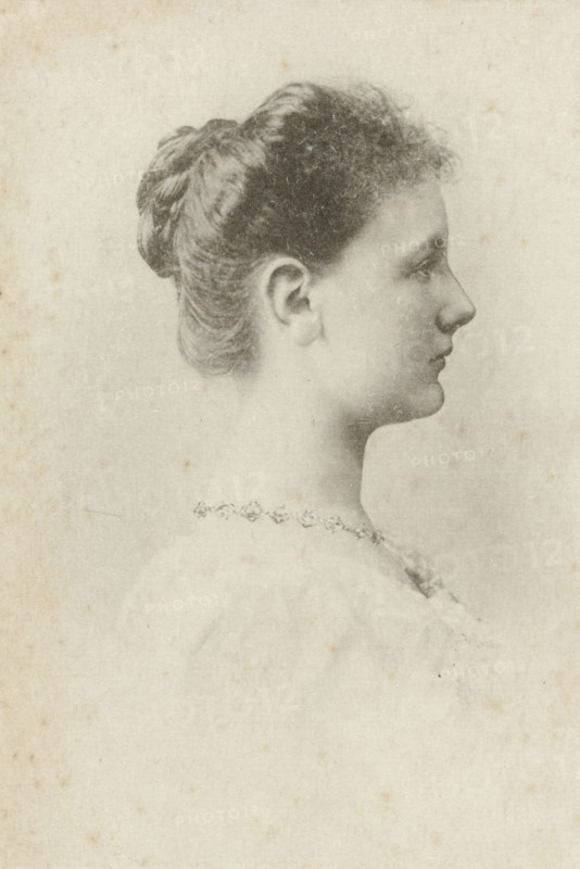 Portrait of Wilhelmina, Queen of the Netherlands, photomechanical print, photographer: Adolphe Zimmermans, cliché maker: anonymous, Netherlands, 1897 - 1899, materials by function, paper, ink, collotype, photoprint and pen in black, height 82 mm x width 56 mm, The title mentioned here refers to the highest title obtained by the sitter, not necessarily to the title that the sitter bears in this performance., Person, Wilhelmina of the Netherlands, A soft-toned profile portrait of a young woman facing right, showing her hair pulled back into a braided bun with short curled bangs at the forehead, a visible ear, a slender neck, and a delicate jawline and nose; she wears a decorative necklace with repeating floral motifs and a light garment at the shoulder, all rendered on a lightly textured, aged paper background.