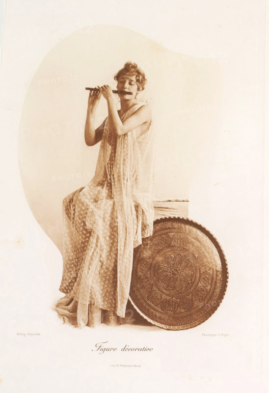 Figure décorative, Woman playing flute with a bowl, page, photomechanical print, photographer: Constant Puyo, France, cliché maker: Paul Dujardin, printer (person): Charles Wittmann, Paris, c. 1886 - in or before 1896, printer (person), paper, photoaquatint, height 211 mm x width 144 mm, transverse flute, adult woman, serving-dish, platter, A sepia-toned portrait of a seated woman wearing a sheer, patterned draped gown and a decorative headband, holding a flute to her lips with both hands and eyes closed, positioned beside a large round ornate tray with embossed geometric and floral designs.