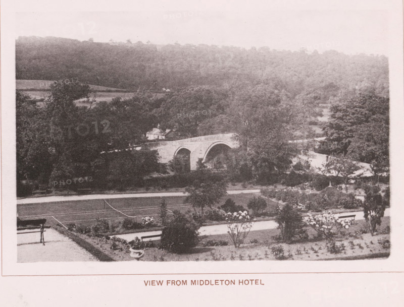 View from Middleton hotel, page, photomechanical print, c. 1890 - c. 1900, paper, collotype, photoprint, height 101 mm x width 153 mm, bridge, A grainy sepia photograph showing a landscape with a stone arched bridge partially obscured by trees, a sloping foreground with planted beds and a bench, expanses of trees and wooded hills in the background, and a small building near the bridge.