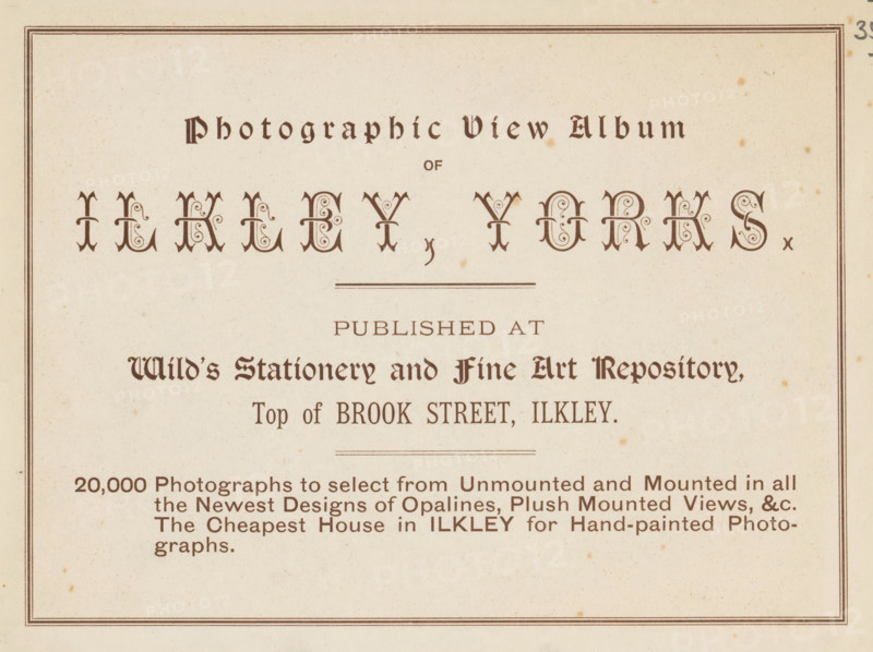 Photographic view album of Ilkley, Yorks, book, inscription: 'ex libris SFJ', publisher: Wild's Stationery and Fine Art Repository, Ilkley, c. 1900, Wild's Stationery and Fine Art Repository, Yorkshire, textile materials, pasteboard, paper, linen (material), printing, collotype, height 157 mm x width 201 mm x thickness 4 mm, A cream colored page with a double-lined rectangular border containing decorative dark brown ornamental headings and stylized lettering, ornate drop-cap style characters arranged near the top, thin horizontal rule lines, a block of smaller dark brown serif text lines in the middle and lower areas, and scattered small brown speckles and age spots across the paper.