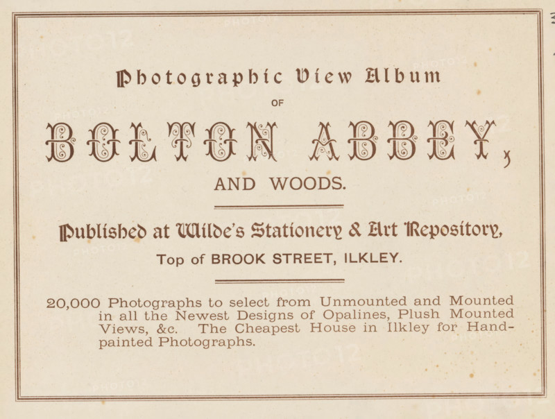Photographic view album of Bolton Abbey and woods, book, inscription: 'ex libris SFJ', publisher: Wild's Stationery and Fine Art Repository, Ilkley, c. 1900, Wild's Stationery and Fine Art Repository, Yorkshire, textile materials, pasteboard, paper, linen (material), printing, collotype, height 157 mm x width 201 mm x thickness 4 mm, A rectangular off-white page with a thin double-lined border and ornate dark brown decorative lettering across the top and center, ornamental flourishes within the larger centered letters, several horizontal rule lines separating sections, a block of smaller dark brown serif text in the lower half arranged in lines, and small scattered brown age spots across the paper.