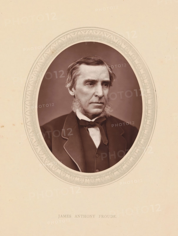 James Anthony Froude, page, photomechanical print, photographer: Lock & Whitfield, cliché maker: anonymous, c. 1871 - in or before 1876, paper, Woodburytype, height 115 mm x width 89 mm, Person, writer, poet, author, historical persons (portraits and scenes from the life) ((full) bust portrait), A sepia-toned oval portrait of an older man with sideburns and short swept hair set against a plain background, mounted on a light cardstock with a decorative oval border around the portrait; the man wears a dark suit jacket with contrasting piping, a waistcoat, a white shirt, and a bow tie, and his expression is neutral as he looks slightly to the side.