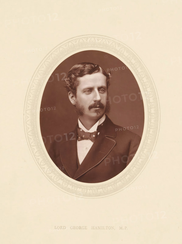 Lord George Hamilton, MP, page, photomechanical print, photographer: Lock & Whitfield, cliché maker: anonymous, c. 1871 - in or before 1876, paper, Woodburytype, height 115 mm x width 89 mm, Person, politician, eg party leader, historical persons (portraits and scenes from the life) ((full) bust portrait), An oval sepia portrait of a man is centered on a pale background with a decorative oval border around the photograph; the man has wavy hair, sideburns, a mustache, and a somber expression, and he is shown from the chest up wearing a dark suit jacket with light piping, a high-collared shirt, and a patterned bow tie.