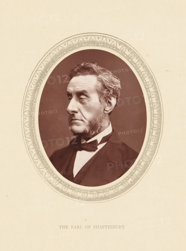 The earl of Shaftesbury, page, photomechanical print, photographer: Lock & Whitfield, cliché maker: anonymous, c. 1871 - in or before 1876, paper, Woodburytype, Woodbury Process, height 115 mm x width 89 mm, Person, Anthony Ashley Cooper, politician, eg party leader, historical persons (portraits and scenes from the life) ((full) bust portrait), An oval sepia portrait of an older man shown in three-quarter profile facing left, with neatly combed hair and prominent sideburns, wearing a dark suit jacket, waistcoat, white shirt, and bow tie, set against a dark background and surrounded by an ornate decorative oval frame on a light textured paper.
