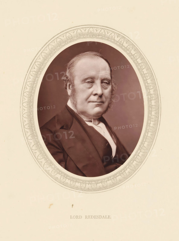 Lord Redesdale, page, photomechanical print, photographer: Lock & Whitfield, cliché maker: anonymous, c. 1871 - in or before 1876, paper, Woodburytype, Woodbury Process, height 115 mm x width 89 mm, Person, John Freeman-Mitford, politician, eg party leader, historical persons (portraits and scenes from the life) ((full) bust portrait), An oval portrait framed by an intricate decorative border shows a middle-aged man with a receding hairline and sideburns wearing a dark suit jacket and a white collar; he faces slightly toward the viewer with a neutral expression, and the background inside the oval is a muted, even tone.