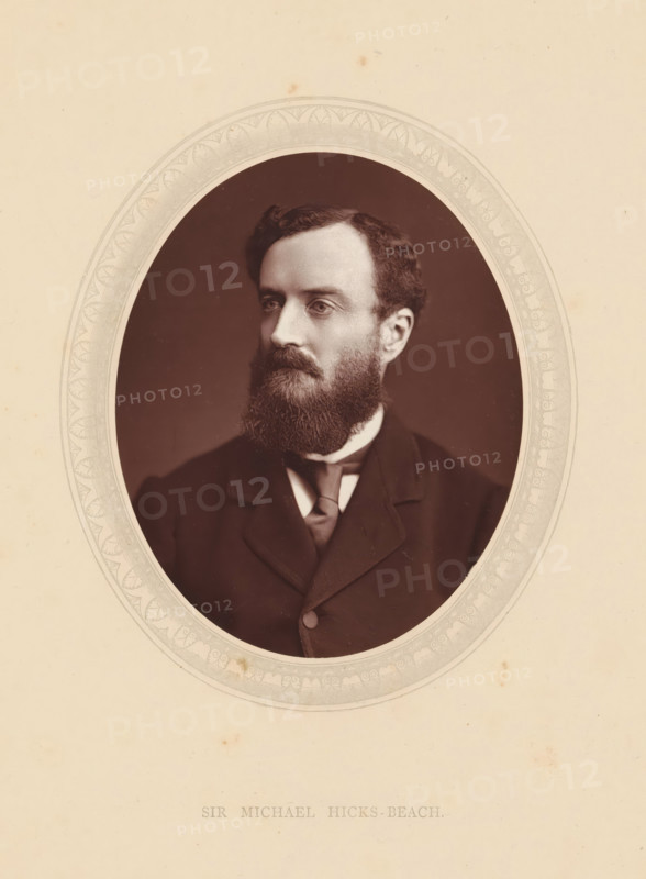 Sir Michael Hicks-Beach, page, photomechanical print, photographer: Lock & Whitfield, cliché maker: anonymous, c. 1871 - in or before 1876, paper, Woodburytype, height 115 mm x width 89 mm, Person, Michael Edward Hicks Beach, politician, eg party leader, historical persons (portraits and scenes from the life) ((full) bust portrait), An oval sepia photograph of a man with dark hair and a full beard set against a dark background, framed by an ornate pale border on a light cream sheet, showing the man in a dark suit jacket with a high collar and a necktie, his gaze directed slightly to one side.