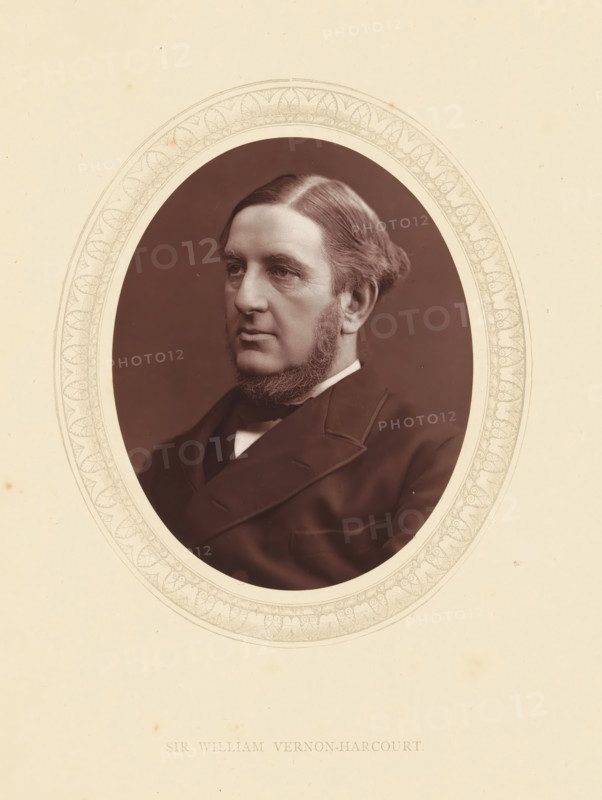 Sir William Vernon-Harcourt, page, photomechanical print, photographer: Lock & Whitfield, cliché maker: anonymous, c. 1871 - in or before 1876, paper, Woodburytype, Woodbury Process, height 115 mm x width 89 mm, Person, William Vernon Harcourt, lawyer, attorney at law, historical persons (portraits and scenes from the life) ((full) bust portrait), A sepia-toned oval portrait of a middle-aged man shown from the shoulders up, set against a dark background and surrounded by a decorative oval mat with a repeating leaf-like pattern, the man has a side-parted hairstyle with hair combed back and sideburns that connect to a trimmed beard along his jaw, his facial expression is neutral with a slightly downturned mouth and he is dressed in a dark formal coat and white collar visible at the neckline.