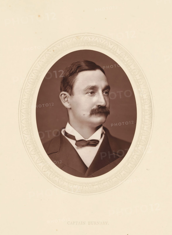 Captain Burnaby, page, photomechanical print, photographer: Lock & Whitfield, cliché maker: anonymous, c. 1871 - in or before 1876, paper, Woodburytype, Woodbury Process, height 115 mm x width 89 mm, Person, Frederick Gustavus Burnaby, officer, historical persons (portraits and scenes from the life) ((full) bust portrait), An oval sepia portrait of a man set against a patterned oval mat within a light beige background, showing a head-and-shoulders view of a man with neatly combed dark hair, a full mustache, and a high collared shirt with a bow tie and a dark jacket, the man looking slightly to the side with a neutral expression.