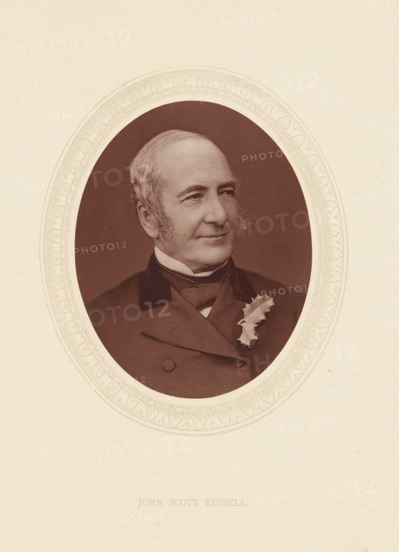 John Scott Russell, page, photomechanical print, photographer: Lock & Whitfield, cliché maker: anonymous, c. 1873 - in or before 1878, paper, Woodburytype, Woodbury Process, height 115 mm x width 89 mm, Person, shipbuilding industry, historical persons (portraits and scenes from the life) ((full) bust portrait), An oval sepia portrait of an older man with light hair and sideburns, shown from the chest up, wearing a dark double-breasted coat with a high collar and a bow at the neck, a light-colored shirt or cravat visible at the collar, and a sprig of holly pinned to his lapel; the portrait is set against a dark background and surrounded by a decorative light-colored oval mat with an ornate patterned border, all on a pale cream sheet.