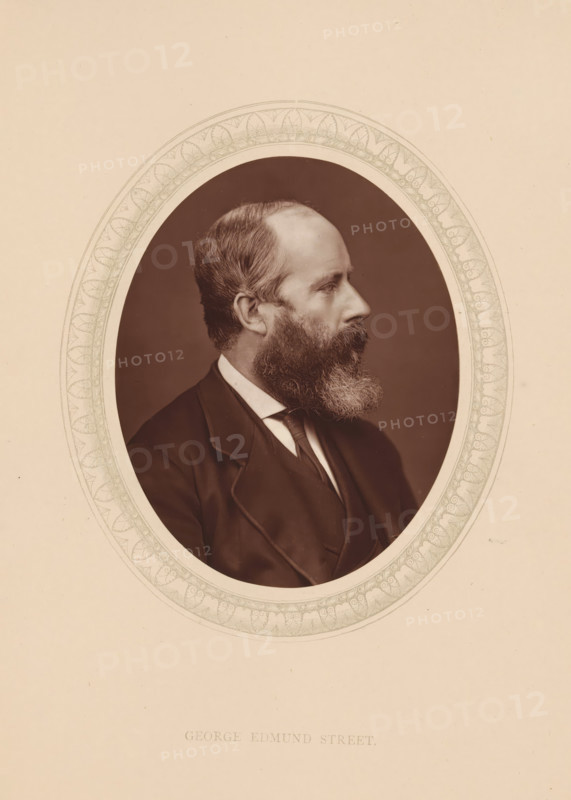 George Edmund Street, page, photomechanical print, photographer: Lock & Whitfield, cliché maker: anonymous, c. 1873 - in or before 1878, paper, Woodburytype, Woodbury Process, height 115 mm x width 89 mm, Person, scholar, philosopher, historical persons (portraits and scenes from the life) ((full) bust portrait), A sepia portrait of a bearded man in profile facing right, shown from the shoulders up within an oval frame that has a decorative patterned border, the man wearing a dark jacket, vest, and a light-colored shirt with a tie, his hair is short and swept back, and his full beard is neatly groomed.