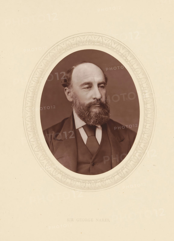 Sir George Nares, page, photomechanical print, photographer: Lock & Whitfield, cliché maker: anonymous, c. 1873 - in or before 1878, paper, Woodburytype, Woodbury Process, height 115 mm x width 89 mm, Person, George Nares, officer, historical persons (portraits and scenes from the life) ((full) bust portrait), An oval sepia photograph of a middle-aged man with a full beard and receding hairline set within an ornate etched oval border on a pale background, showing the man in a dark suit jacket, waistcoat, and tie, his head turned slightly to the side and his expression neutral, with visible facial features including a beard, mustache, ears, and short hair, and the etched border featuring repeating decorative motifs.
