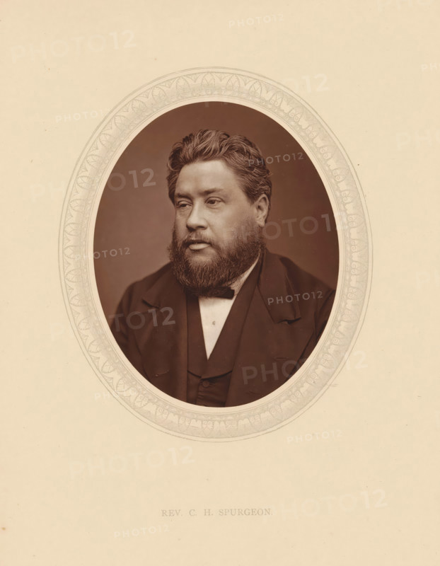 Rev. CH Spurgeon, page, photomechanical print, photographer: Lock & Whitfield, cliché maker: anonymous, c. 1875 - in or before 1880, paper, Woodburytype, Woodbury Process, height 115 mm x width 89 mm, Person, Charles Haddon Spurgeon, theologian, historical persons (portraits and scenes from the life) ((full) bust portrait), An oval sepia photograph of a man with wavy hair and a full beard set within a decorative oval border on a light beige background, the man wearing a dark jacket, waistcoat, and bow tie, looking slightly to his left with a neutral expression.